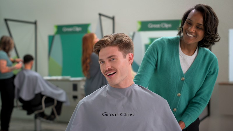 A man smiling into a mirror at a Great Clips salon.